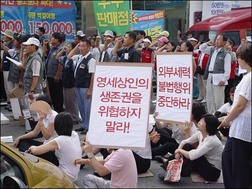 불매운동 구호를 외치는 참여단체와 '생존권 보장'을 요구하는 입점업자들의 모습이 대조된다. 